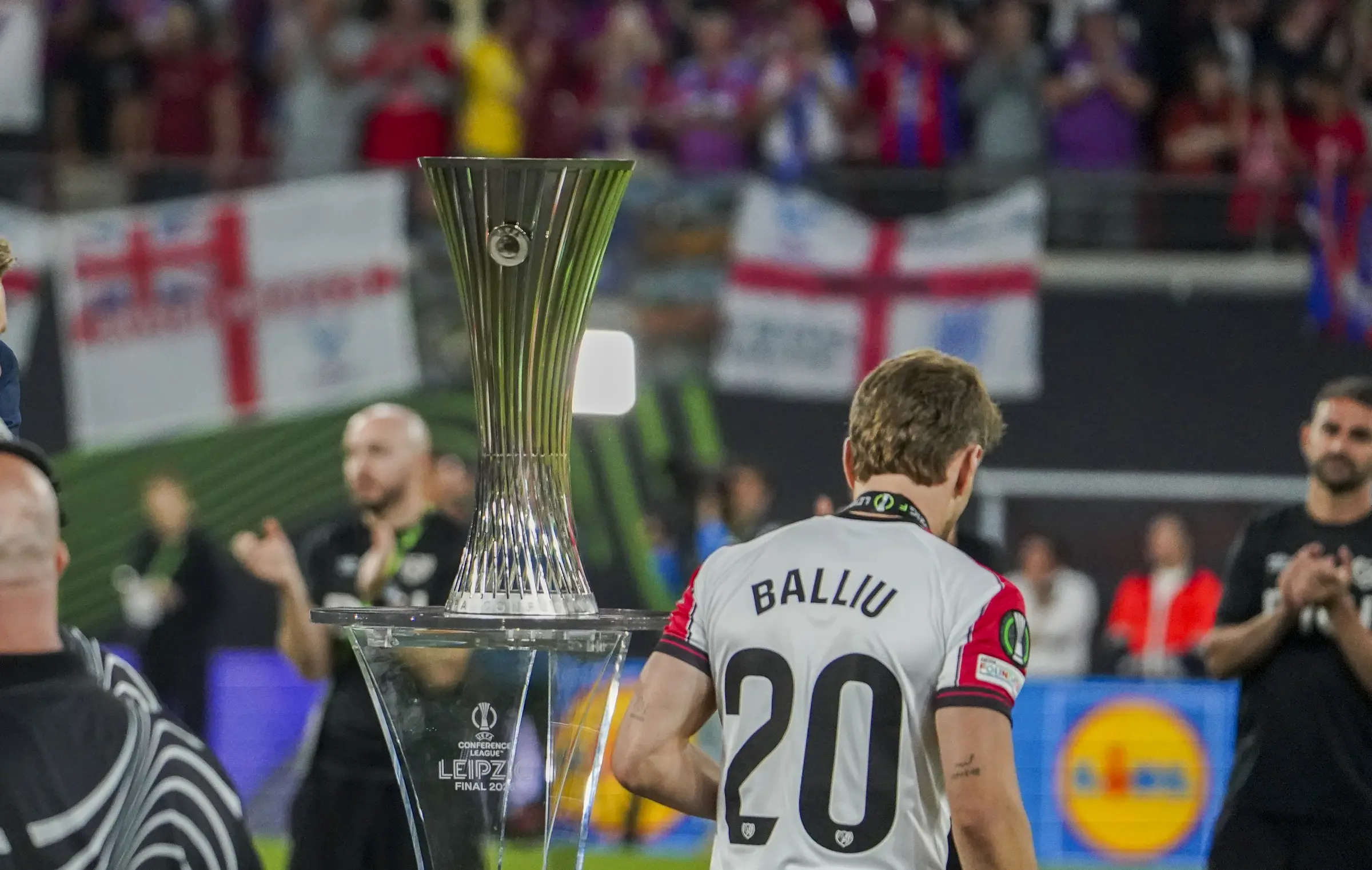 The Conference League trophy stands in the foreground as a Rayo Vallecano player walks away.