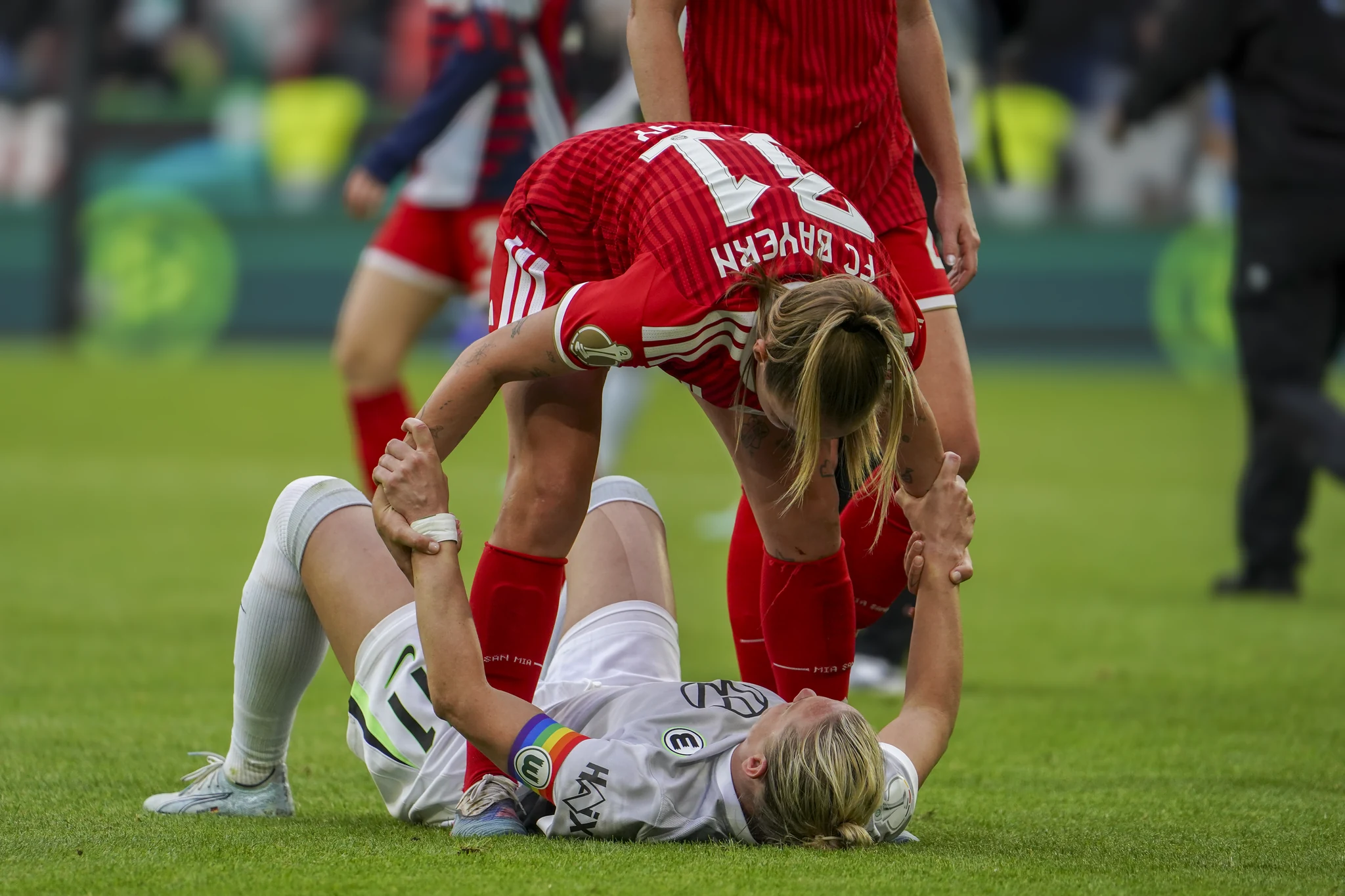 A Bayern player reaches down to a seated Wolfsburg opponent.
